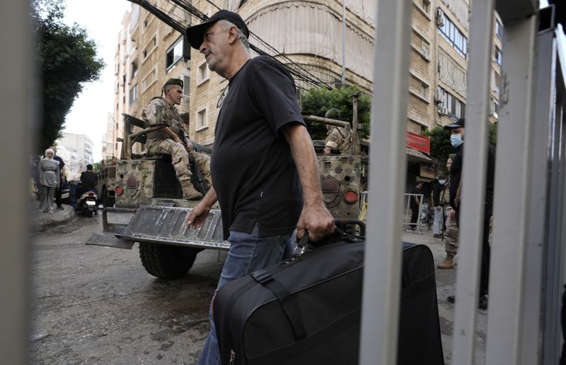 A man walks with a suitcase as Lebanese soldiers drive near the site of Friday's Israeli strike in Beirut's southern suburb, Sunday, Sept. 22, 2024. (AP Photo/Bilal Hussein)