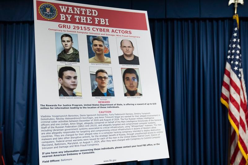 A graphic of the Russian suspects wanted by the FBI involved in a conspiracy to commit criminal cyber activities against Ukrainian government systems is displayed during a news conference at the Office of the United States Attorney in Baltimore, Thursday, Sept. 5, 2024. (AP Photo/Stephanie Scarbrough)