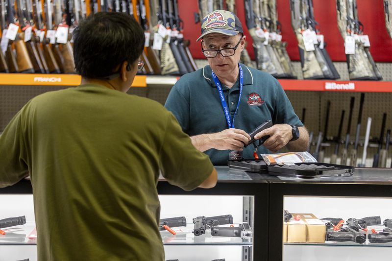 Adventure Outdoors employee John Faber helps Lu Li with his new gun purchase in Smyrna on Tuesday.