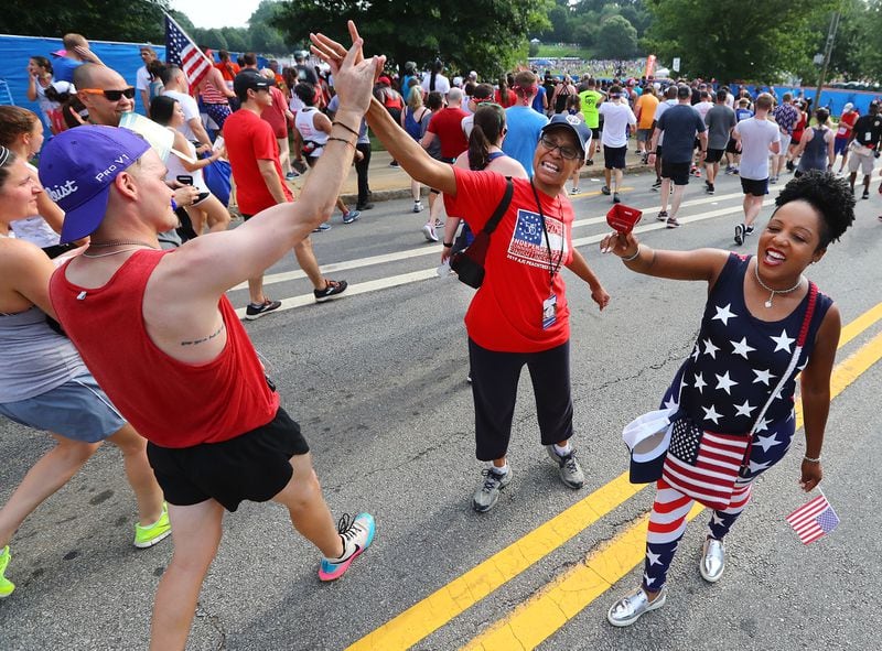 Volunteers Renita Humphrey (center) and Tammi Perkins (right) encourage runners with high fives and cheers after the finish line during the 50th AJC Peachtree Road Race on Thursday, July 4, 2019, in Atlanta.  Curtis Compton/ccompton@ajc.com