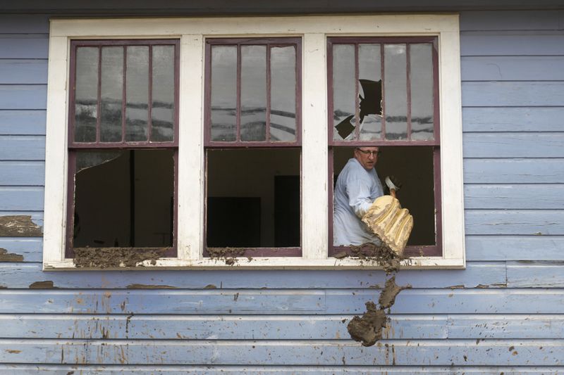 Ben Phillips scoops mud out a window of his house left in the wake of Hurricane Helene, Tuesday, Oct. 1, 2024, in Marshall, N.C. (AP Photo/Jeff Roberson)