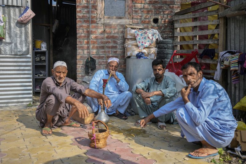 FILE- An elderly man smokes a hookah pipe as he sits with other men outside a polling station during the second phase of the assembly election in the interior of Dal Lake in Srinagar, Indian controlled Kashmir, Sept. 25, 2024.(AP Photo/Mukhtar Khan, File)