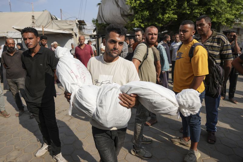 A Palestinian carries a body at the funeral for more than 15 people, including several children and women, killed in an Israeli strike, at Al-Aqsa Martyrs Hospital in Deir al-Balah, Gaza Strip, Saturday, Aug. 17, 2024. The strike hit a house and an adjacent warehouse sheltering displaced people at the entrance of the town of Zawaida, according to the hospital where the casualties were taken. (AP Photo/Abdel Kareem Hana)