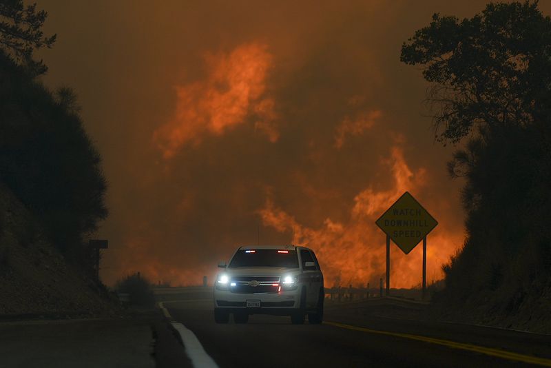 FILE - The Line Fire jumps Highway 330 as an emergency vehicle is driven past Saturday, Sept. 7, 2024, near Running Springs, Calif. (AP Photo/Eric Thayer, File)