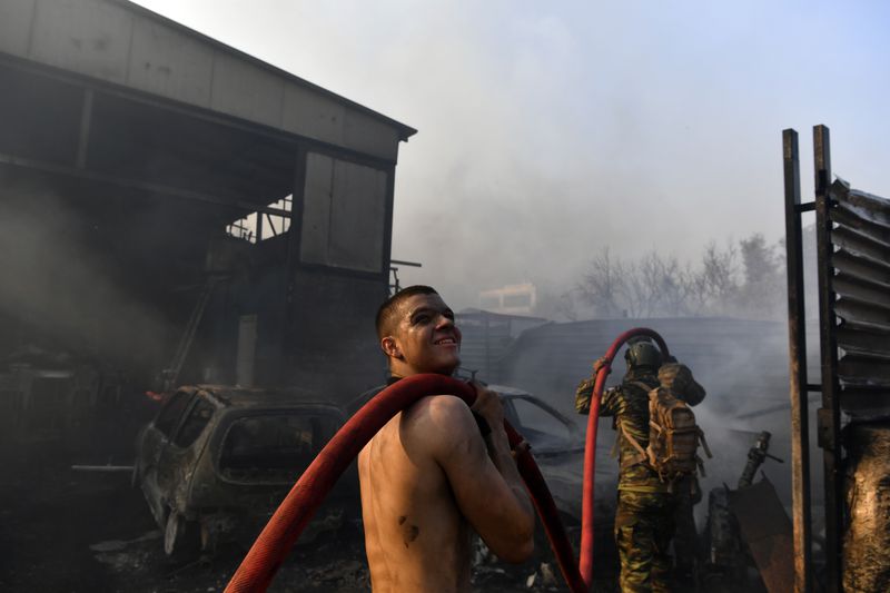 Two men try to extinguish the flames at a burning business during a fire in northern Athens, Monday, Aug. 12, 2024, as hundreds of firefighters tackle a major wildfire raging out of control on fringes of Greek capital. (AP Photo/Michael Varaklas)