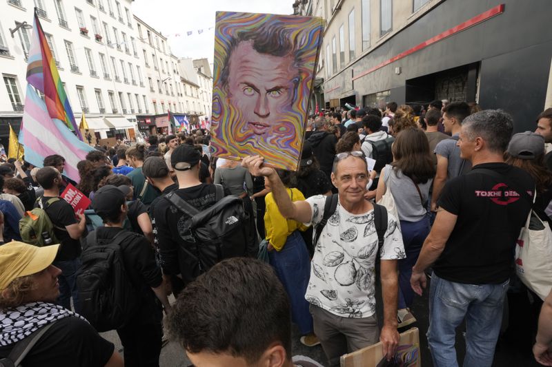 A demonstrator holds a poster featuring French President Emmanuel Macron during a protest, responding to a call from the far-left party who criticized as a power grab the president's appointment of a conservative new prime minister, Michel Barnier, in Paris, France, Saturday, Sept. 7, 2024. (AP Photo/Michel Euler)