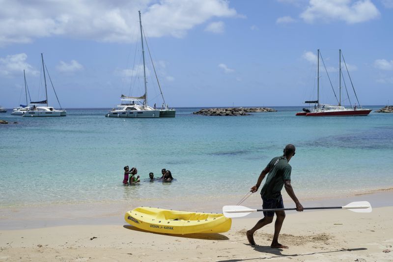 A man pulls a kayak as sailboats line up to enter a marina ahead of Hurricane Beryl's arrival in Speightstown, Barbados, Sunday, June 30, 2024. (AP Photo/Ricardo Mazalan)