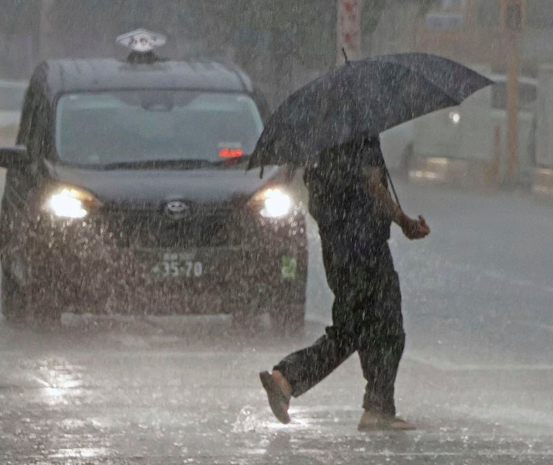 People holding an umbrella crosses a street in the heavy rain in Miyazaki, Miyazaki prefecture, western Japan, Wednesday, Aug. 28, 2024, as a typhoon is approaching. (Kyodo News via AP)