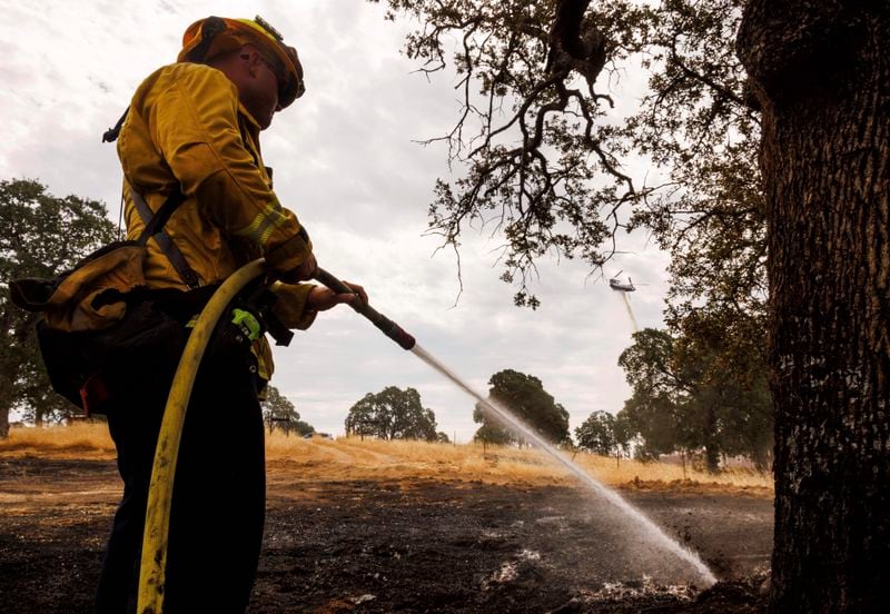 A firefighter uses a hose while a helicopter drops water as the Apache Fire burns in Palermo, Calif., on Tuesday, Jun. 25, 2024. According to Cal Fire, more than a dozen new fires sparked by lightning. (AP Photo/Ethan Swope)
