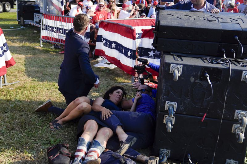 People take cover as U.S. Secret Service agents surround Republican presidential candidate former President Donald Trump on stage at a campaign rally, Saturday, July 13, 2024, in Butler, Pa. (AP Photo/Evan Vucci)