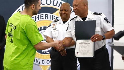 Samuel Santos receives his GED from Cobb County Sheriff Craig Owens as Chief Deputy Rhonda Anderson looks on during a graduation ceremony for inmates at Cobb County Detention Facility in Marietta on Tuesday, May 28, 2024. (Natrice Miller/ AJC)