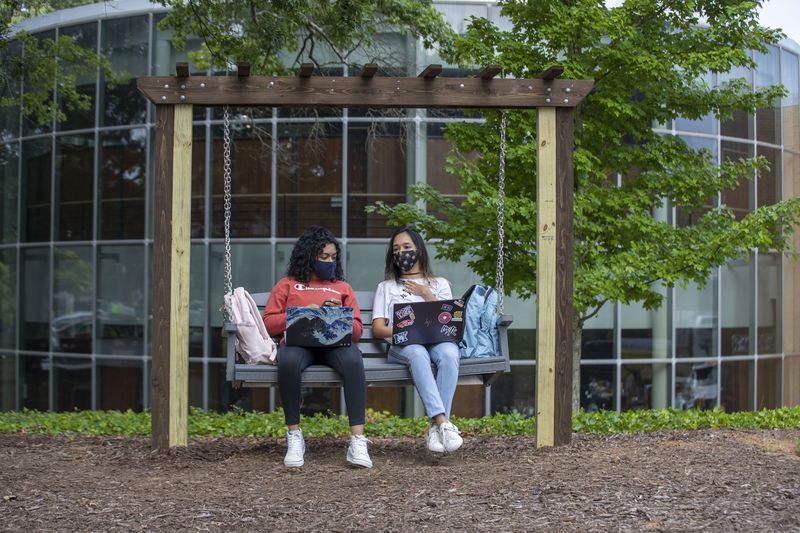 08/17/2020 - Kennesaw, Georgia - Kennesaw State University freshmen Henna Ganesh (left) and Anngie Villlegas (right) wear masks as they socialize on a new bench swing during the first day of classes at Kennesaw State University's main campus in Kennesaw, Monday, August 17, 2020. (ALYSSA POINTER / ALYSSA.POINTER@AJC.COM)