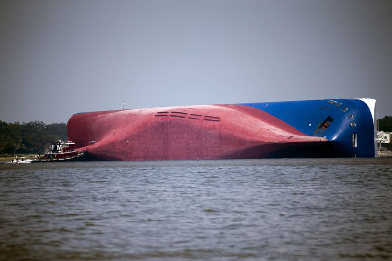 FILE - In this Sept. 9, 2019, file photo, a Moran tugboat nears the stern of the capsizing vessel Golden Ray near St. Simons Sound off the coast of Georgia. The salvage team salvage team is seeking a federal permit to surround the shipwreck with a giant mesh barrier to contain any debris when they cut the ship apart. (AP Photo/Stephen B. Morton, File)