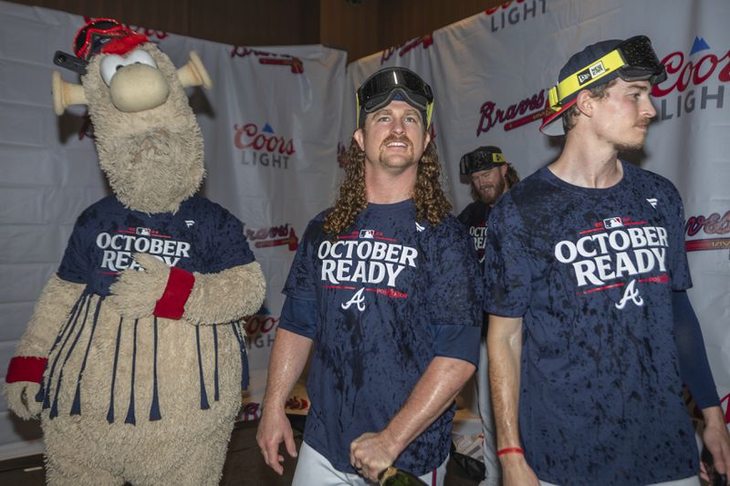 Atlanta Braves mascot Blooper, left, pitcher Grant Holmes, center, and pitcher Max Fried, right, celebrate in the locker room after clinching a wild-card playoff berth after the second baseball game of a doubleheader against the New York Mets, Monday, Sept. 30, 2024, in Atlanta. (AP Photo/Jason Allen)