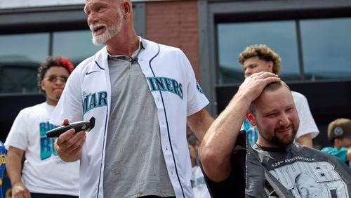 Former Seattle Mariners player Jay Buhner turns and jokes with the crowd as he shaves catcher Cal Raleigh's head on Buhner Buzz Night, Thursday, June 13, 2024, in Seattle. The promotion is based on Buhner's shaved-head style. (AP Photo/John Froschauer)