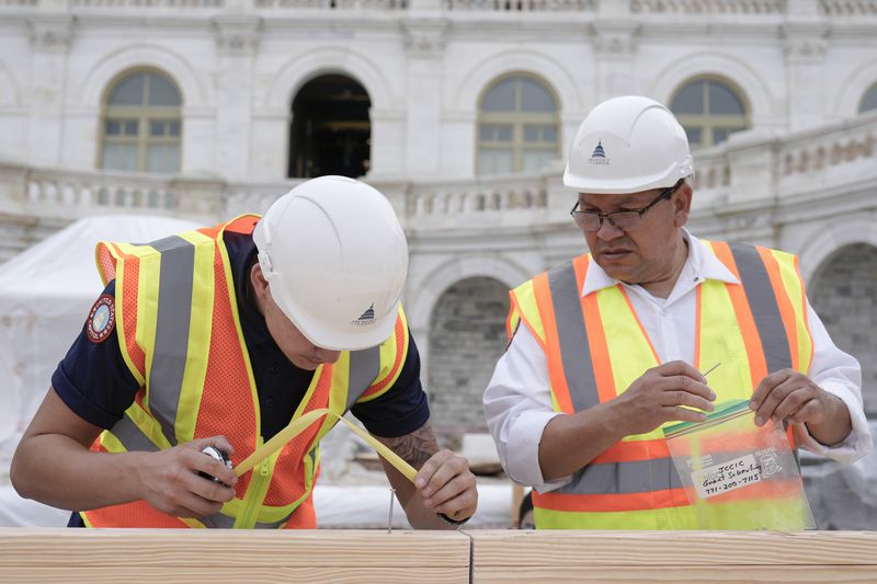 Tyler Smith, a woodcrafter with the Architect of the Capitol, and Herbert Melgar, a painter, measure out the nail placement for Congress members to hammer for the First Nail Ceremony marking the beginning of construction of the 2025 Presidential Inauguration platform at the Capitol, Wednesday, Sept. 18, 2024, in Washington. (AP Photo/Mariam Zuhaib)