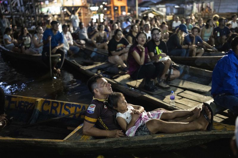 Spectators sit in boats watching a film projected on a screen set up on a wooden structure during the Muyuna Floating Film Festival in the Belen neighborhood of Iquitos, Peru, Saturday, May 25, 2024. (AP Photo/Rodrigo Abd)