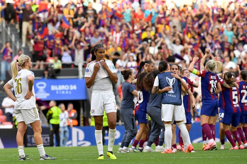 Lyon's Wendie Renard, center, and Lindsey Horan, left, react while Barcelona players celebrate at the end of the women's Champions League final soccer match between FC Barcelona and Olympique Lyonnais at the San Mames stadium in Bilbao, Spain, Saturday, May 25, 2024. Barcelona won 2-0. (AP Photo/Alvaro Barrientos)