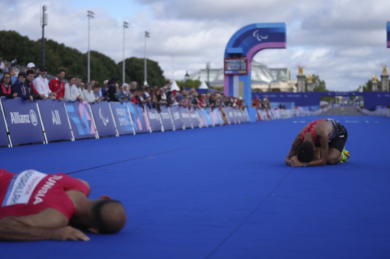 Japan's Tadashi Horikoshi, right, and Tunisia's Hatem Nasrallah lie on the ground after the men's marathon T12 at the 2024 Paralympics, Sunday, Sept. 8, 2024, in Paris, France. (AP Photo/Thibault Camus)