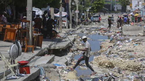 A man crosses a storm drain filled with trash in Port-au-Prince, Haiti, Friday, Sept. 13, 2024. (AP Photo/Odelyn Joseph)