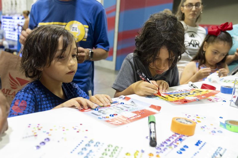Evan, left, and Gabe Matisoff decorate Atlanta Journal-Constitution Peachtree Road Race bibs during the Peachtree Health and Fitness Expo in Atlanta on Tuesday, July 2, 2024. Evan, 8, was decorating his mom’s bib while Gabe, 11, was decorating his own.   (Ben Gray / Ben@BenGray.com)
