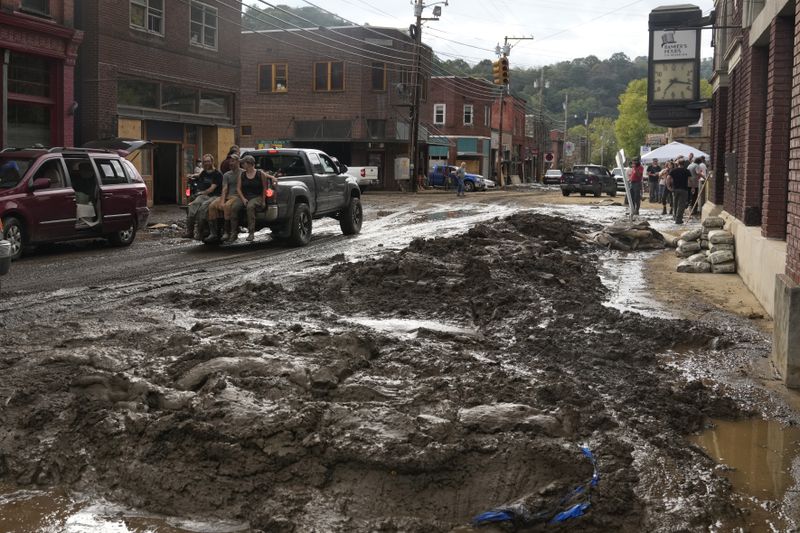 People ride in the back of a pickup truck on a street left covered in deep mud in the aftermath of Hurricane Helene Tuesday, Oct. 1, 2024, in Marshall, N.C. (AP Photo/Jeff Roberson)