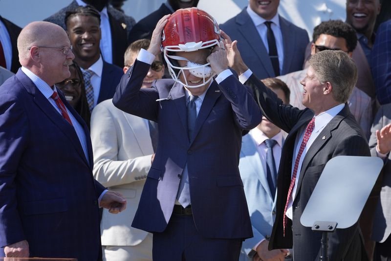 Kansas City Chiefs coach Andy Reid, left, and CEO Clark Hunt, right, watch as President Joe Biden, center, puts on a Chiefs helmet during an event with the Super Bowl-champion Kansas City Chiefs on the South Lawn of the White House, Friday, May 31, 2024, to celebrate their championship season and victory in Super Bowl LVIII. (AP Photo/Evan Vucci)