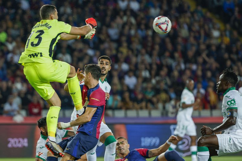 Getafe's goalkeeper David Soria, top, makes a save in front of Barcelona's Robert Lewandowski during a Spanish La Liga soccer match between Barcelona and Getafe at the Olympic stadium in Barcelona, Spain, Wednesday, Sept. 25, 2024. (AP Photo/Joan Monfort)