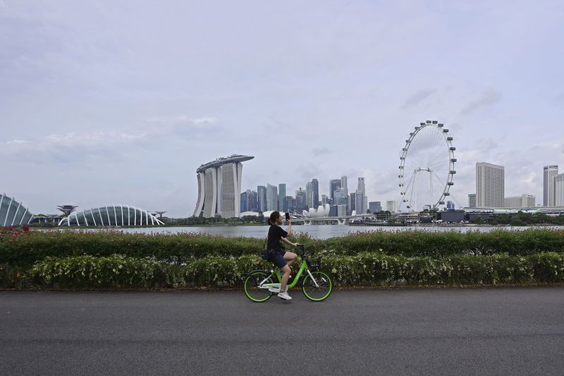 A cyclist takes photo of the city skyline in Singapore, Sunday, Sept. 8, 2024. (AP Photo/Suhaimi Abdullah)