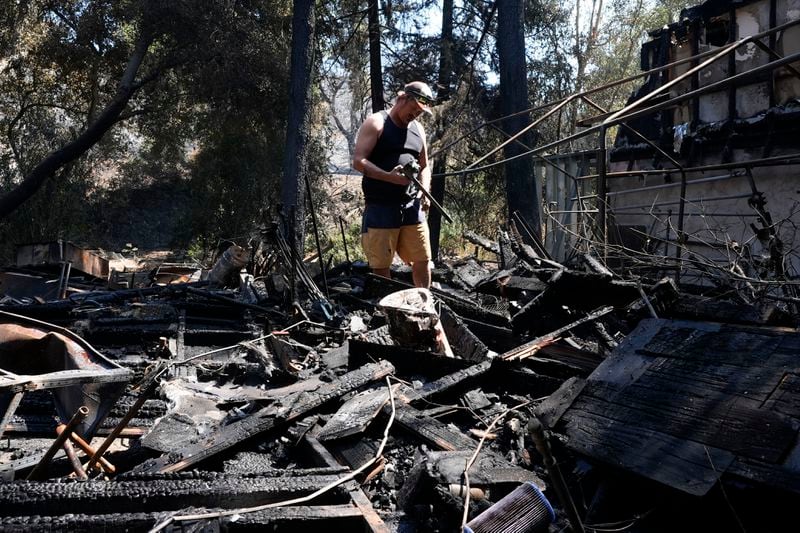 Matt Howe sifts through his partially damaged property after the Airport Fire swept through Thursday, Sept. 12, 2024, in El Cariso Village, in unincorporated Riverside County, Calif. (AP Photo/Gregory Bull)