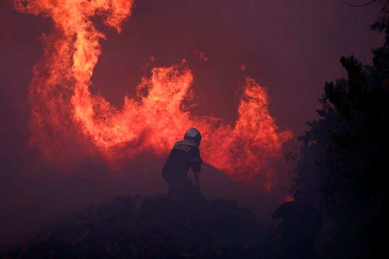 A firefighter tries to extinguish the flames at a business during a fire in northern Athens, Monday, Aug. 12, 2024, as hundreds of firefighters tackle a major wildfire raging out of control on fringes of Greek capital. (AP Photo/Aggelos Barai)