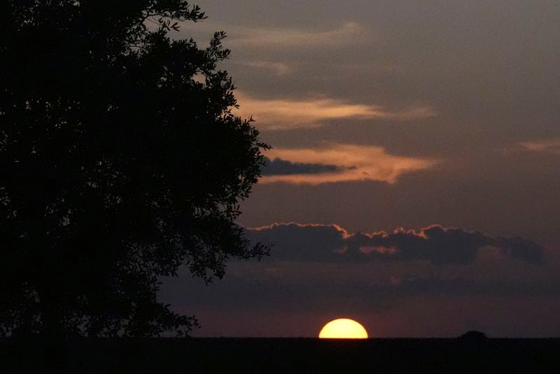 The sun sets in the Florida Everglades as hunters wait for dark to search for invasive Burmese pythons, Tuesday, Aug. 13, 2024, in the Florida Everglades. (AP Photo/Wilfredo Lee)