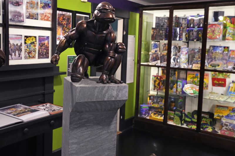 A bronze sculpture of the Teenage Mutant Ninja Turtle character "Raphael" is displayed along with comic books and memorabilia in a permanent collection at the Woodman Museum, Thursday, Sept. 5, 2024, in Dover, N.H. (AP Photo/Charles Krupa)