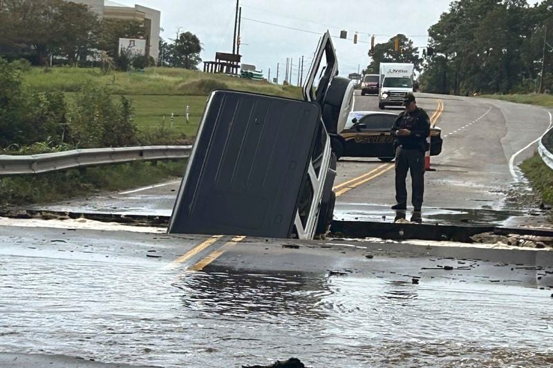 This photo provided by Brunswick County Sheriff's Office shows a police officer checking on a vehicle that fell into a sinkhole on a highway in Brunswick County, N.C., after a storm dropped historic amounts of rain, Monday, Sept. 16, 2024. (Brunswick County Sheriff's Office via AP)