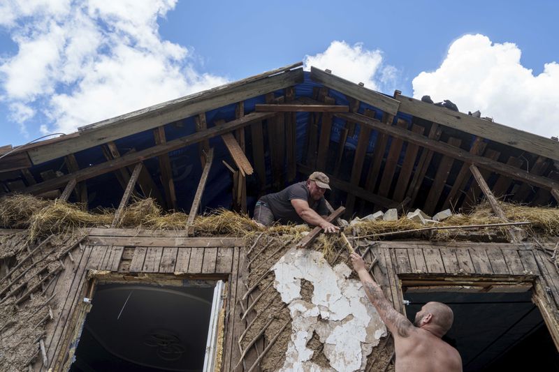 People cover a roof with tarps after their house was hit by a Russian airstrike near the Russian-Ukrainian border in Sumy region, Ukraine, Thursday, Aug. 15, 2024. (AP Photo/Evgeniy Maloletka)