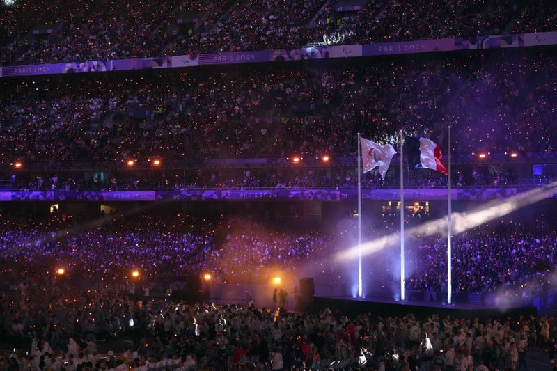 The Paralympic flag flutters next to the French flag during the closing ceremony of the 2024 Paralympics, Sunday, Sept. 8, 2024, in Paris, France. (AP Photo/Thibault Camus)