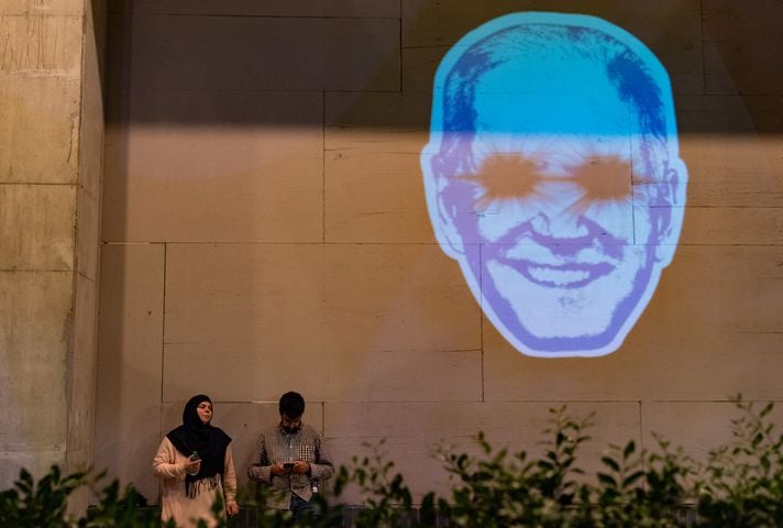 Pro-Palestine protesters rest by a projected image of President Joe Biden as “Dark Brandon” near the intersection of 10th Street NW and Spring Street NW in Atlanta on Thursday, June 27, 2024. Nearby, President Biden and former President Donald Trump participated in a debate hosted by CNN. (Seeger Gray / AJC)