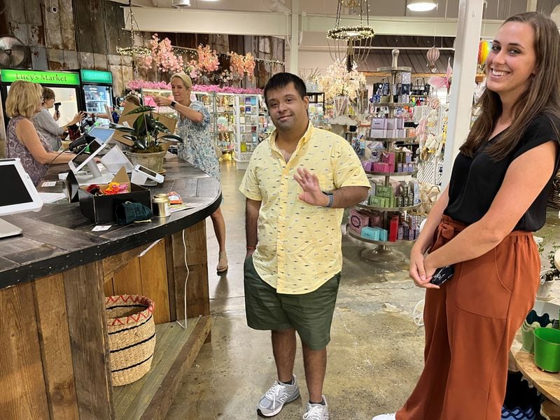 Angad Sahgal (center), who has Down syndrome, has been making cold calls to metro Atlanta stores each week, looking for retailers willing to stock teas imported by his Sandy Springs-based business, Chai Ho Tea. Job coach Caroline Kramer (right) helped on a recent trip he made to Lucy’s Market in Buckhead where he pitched his products. (Matt Kempner / mkempner@ajc.com )