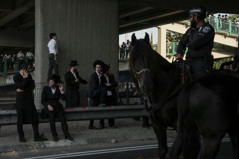 Israeli mounted police officers stand next to ultra-Orthodox Jewish men blocking a highway during a protest against army recruitment in Bnei Brak, Israel, Thursday, June 27, 2024. Israel's Supreme Court unanimously ordered the government to begin drafting ultra-Orthodox Jewish men into the army — a landmark ruling seeking to end a system that has allowed them to avoid enlistment into compulsory military service. (AP Photo/Oded Balilty)