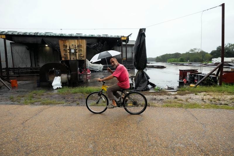 Kevin "Choupie" Badle, 67, rides his bike with an umbrella to buy more cigarettes at the store ahead of Hurricane Francine, expected to make landfall this evening, in Stephenville, La., Wednesday, Sept. 11, 2024. (AP Photo/Gerald Herbert)