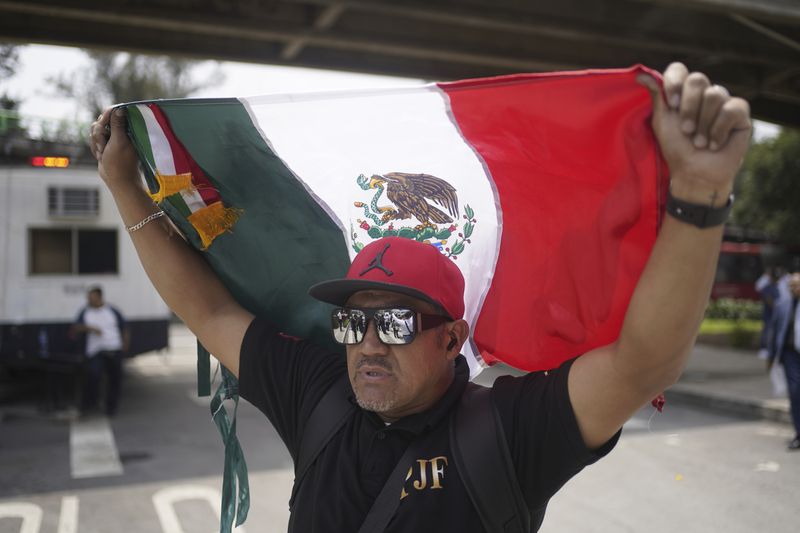 Judicial worker Marcos Arenas holds up a Mexican flag during a protest against constitutional reform proposals that would make judges stand for election, outside a sports center where lawmakers are meeting as an alternative due to other demonstrators blocking Congress in Mexico City, Tuesday, Sept. 3, 2024. (AP Photo/Felix Marquez)