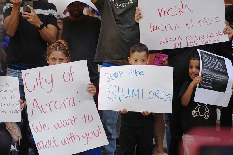 Residents hold up placards during a rally staged by the East Colfax Community Collective to address chronic problems in the apartment buildings occupied by people displaced from their home countries in central and South America Tuesday, Sept. 3, 2024, in Aurora, Colo. (AP Photo/David Zalubowski)