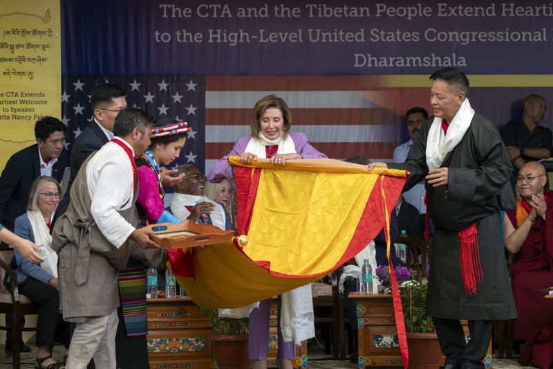 Democratic former House Speaker Nancy Pelosi, center, is presented with a Tibetan traditional Buddhist painting called Thangka by the President of the Central Tibetan Administration, Penpa Tsering, right, at a public event during which a US delegation led by Republican Rep. Michael McCaul was felicitated by Tibetan exiled government officials at the Tsuglakhang temple in Dharamshala, India, Wednesday, June 19, 2024. (AP Photo/Ashwini Bhatia)