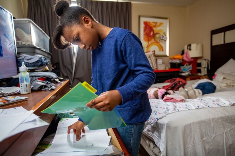 The White family lives in an extended-stay hotel where parents Melvin and Raneice live with five of their children on Wednesday, Dec 21, 2022.   Mckenzie, 10, organizes her notebook with some of her drawings and school work while her mom Raneice watches over 5-month-old Justice, and 4-year-old Legend, sleeping, before Melvin and the boys get back from haircuts.  The family has lived in extended-stay hotels for years despite Melvin working full-time they canÕt find long-term safe housing they can afford.  (Jenni Girtman for The Atlanta Journal-Constitution)