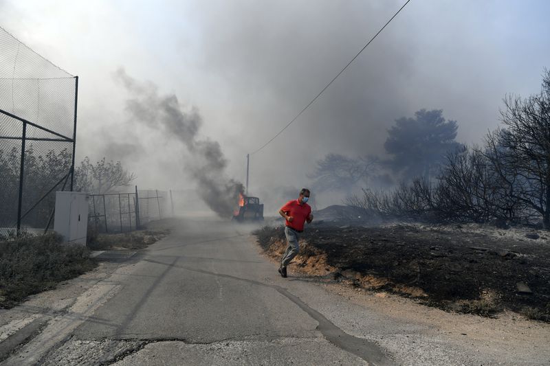 A man runs while flames burn a mini excavator during a fire in northern Athens, Monday, Aug. 12, 2024, as hundreds of firefighters tackle a major wildfire raging out of control on fringes of Greek capital. (AP Photo/Michael Varaklas)