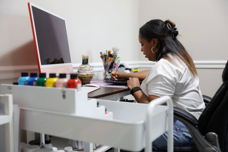 Bria Bowen works on a custom graduation hat for a client in her home office in Kennesaw on Wednesday, April 19, 2023. Bowen charges $140 and up for her caps. (Natrice Miller/natrice.miller@ajc.com)