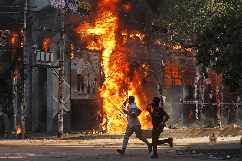 FILE- People run past a shopping center which was set on fire in Dhaka, Bangladesh, Aug. 4, 2024. (AP Photo/Rajib Dhar, File)