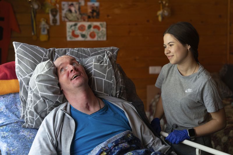 A doctor talks to Vitalii Shumei, 36, a bedridden Ukrainian officer heavily wounded in a battle with Russian forces , at the rehabilitation centre in Modrychi, Western Ukraine, Wednesday, Aug. 28, 2024. (AP Photo/Efrem Lukatsky)