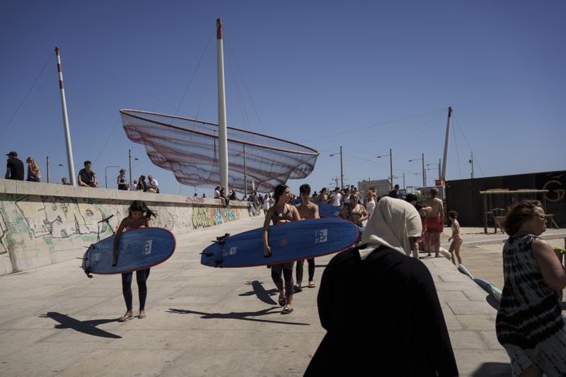 Surf Church members Lais Cardoso, center, and her brother, Ian Cardoso, behind her, carry their surfboards before they catch waves and worship at Matosinhos beach in the suburbs of Porto, Portugal on Sunday, Aug. 18, 2024. (AP Photo/Luis Andres Henao)