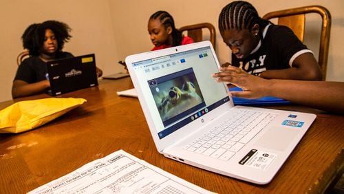 Rakiyah Hill, 10, front right, a 5th grader at McClendon Elementary, learns cell structure on a computer her mother had to buy this month so all children would be able to get their school work done. Raina Hill, 12, back left, a 6th grader at Champion Middle School uses the only DeKalb County computer they have, while Rihanna Hill,13, in red, an 8th grader at Champion Middle School uses a tablet to do school work and sister, Roniyah Hill, black shirt braids,15, a 10th grader at Martin Luther King High School uses her phone to look up definitions.(Jenni Girtman for Atlanta Journal Constitution)